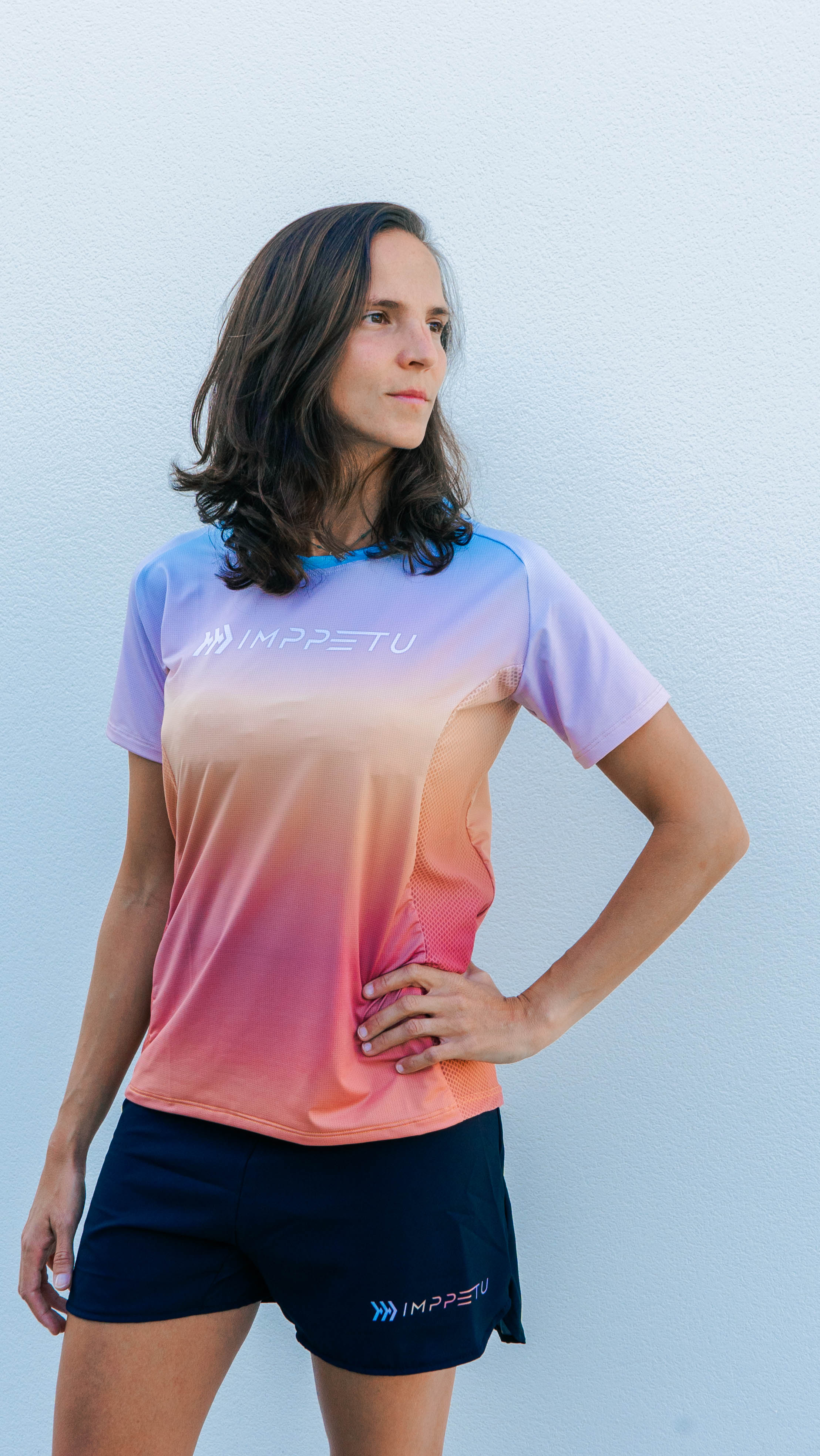 Corredora vistiendo camiseta técnica sostenible IMPPETU en color sunset durante entrenamiento al aire libre. 